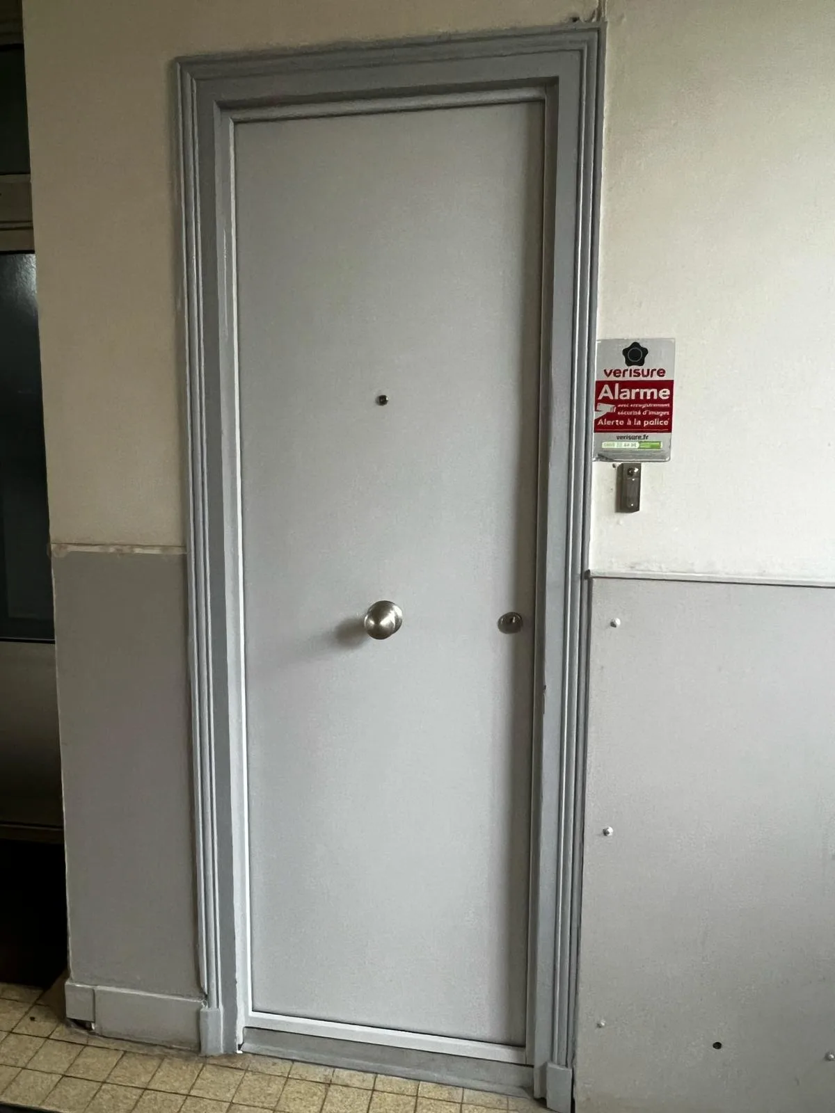 Porte métallique grise dans un local carrelé, rue Le Corbusier à Boulogne-Billancourt, autocollant d'alarme sur le montant