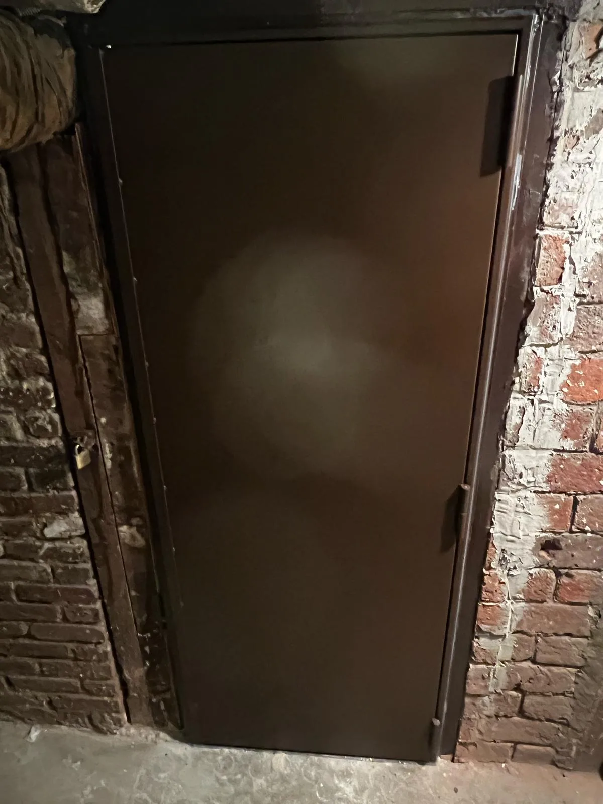 Porte de cave métallique brun foncé encastrée dans un mur de brique brute, place Marcel Sembat à Boulogne-Billancourt