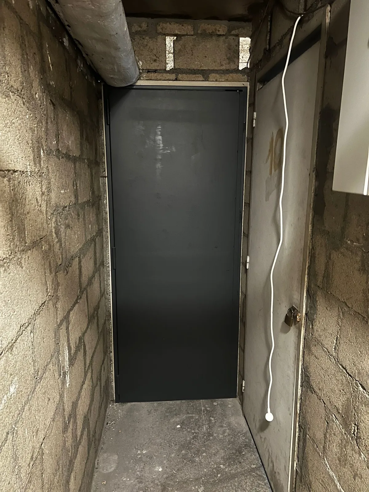 Porte métallique gris foncé au fond d'un couloir de cave en béton brut, allée de la Belle Feuille à Boulogne-Billancourt